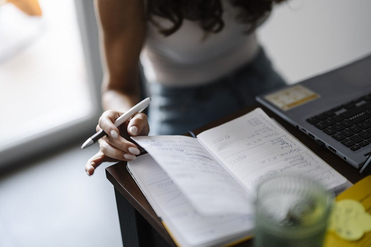 Handwritten notes in a notebook next to a laptop on a desk. Editorial photograph, not a coverage report.